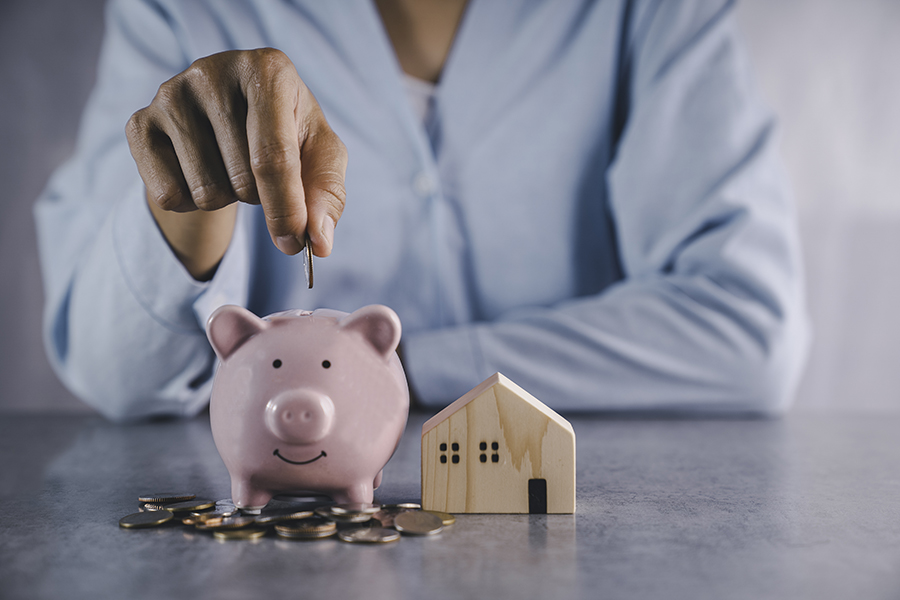 Person saving money in piggy bank and house model.
