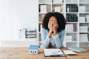 Frustrated woman with paperwork and model house.